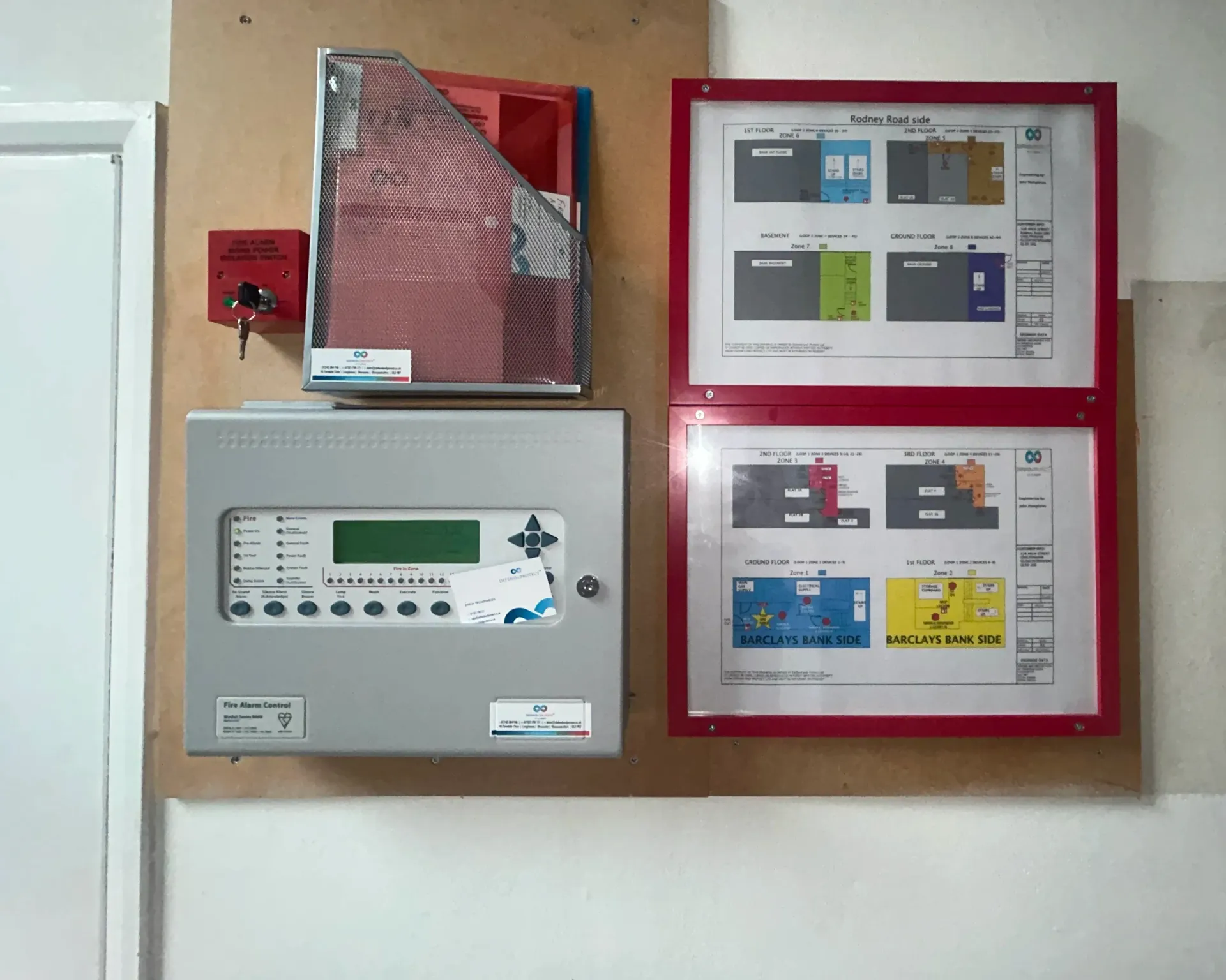 Wall-mounted electrical control panel with switches and display, beside red safety covers and posted instruction sheets.