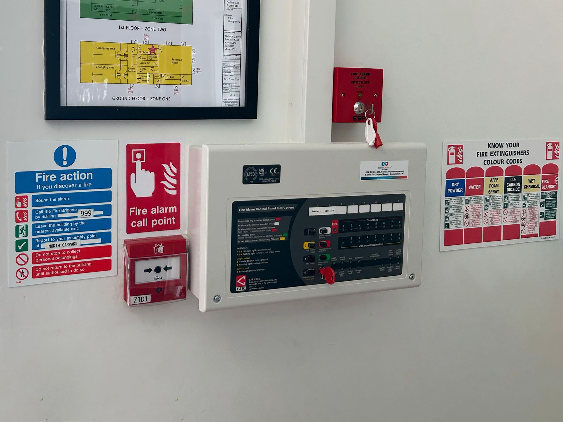 Wall-mounted fire alarm control panel with red emergency switches and safety notices on a white wall.