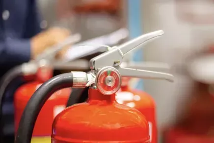 Red fire extinguisher with hose and silver handle in a blurred indoor setting