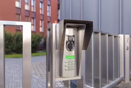 Outdoor access control keypad mounted on a metal gate beside a modern building
