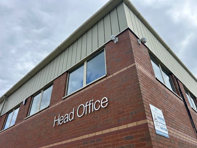 Brick building corner with “Head Office” sign and upper windows under a cloudy sky