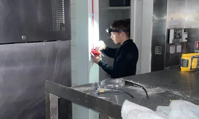 Person in dark clothing holding a red object in an industrial kitchen.