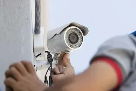 Person installing a white security camera on a wall with a screwdriver
