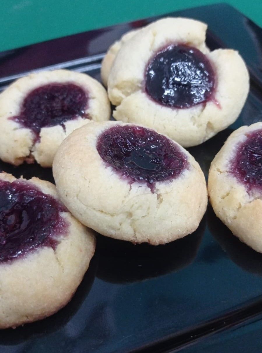Bandeja de galletas redondas con mermelada morada oscura en el centro, sobre un plato negro.