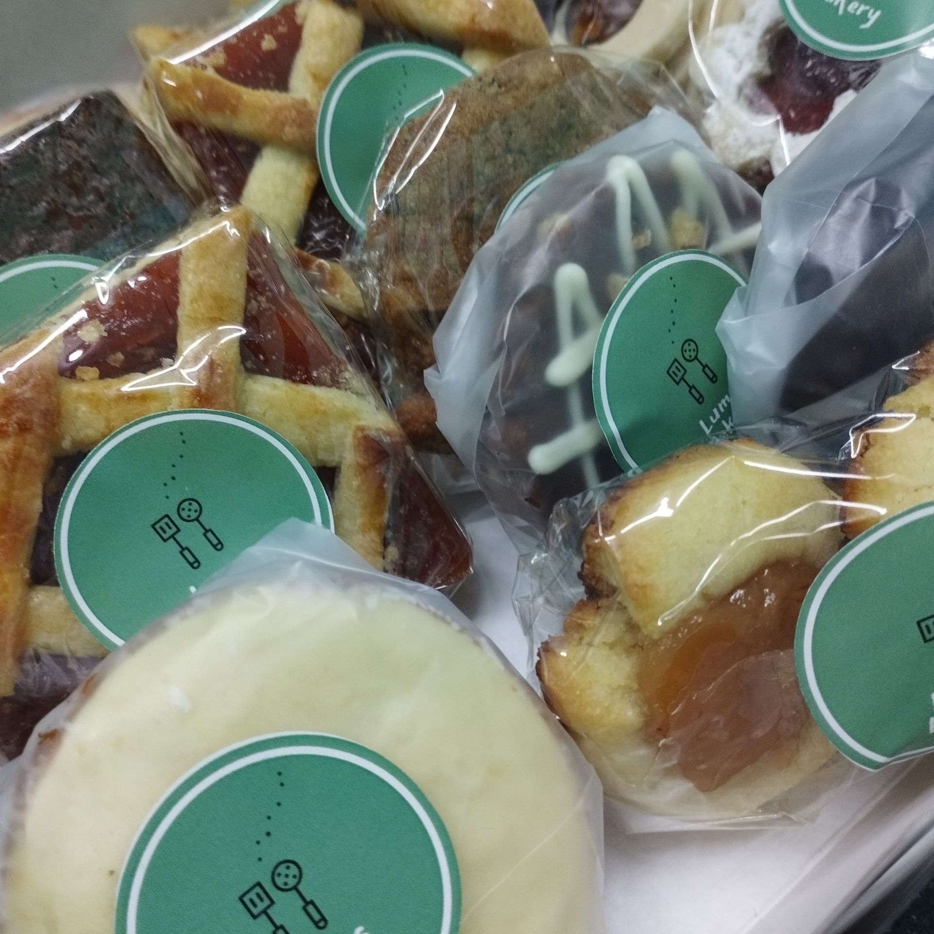 Surtido de aperitivos envasados ​​con etiquetas verdes, que incluyen pasteles y galletas, dispuestos en una bandeja o caja.