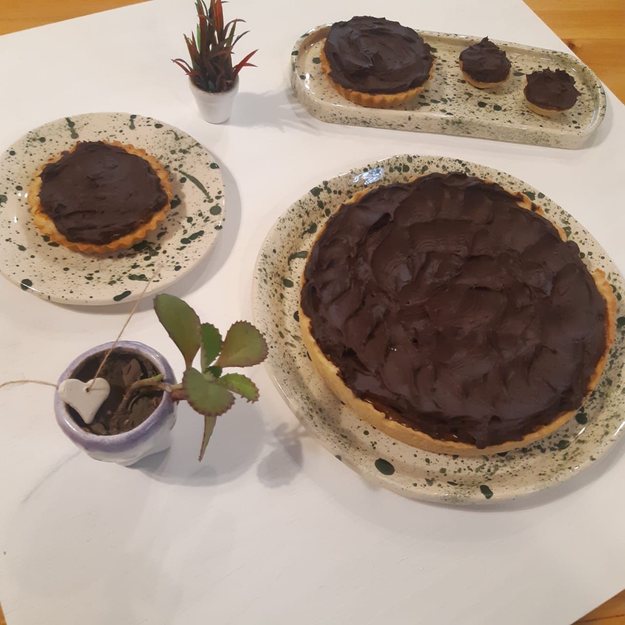 Surtido de postres de chocolate y tartas sobre una mesa blanca con pequeñas plantas en macetas.