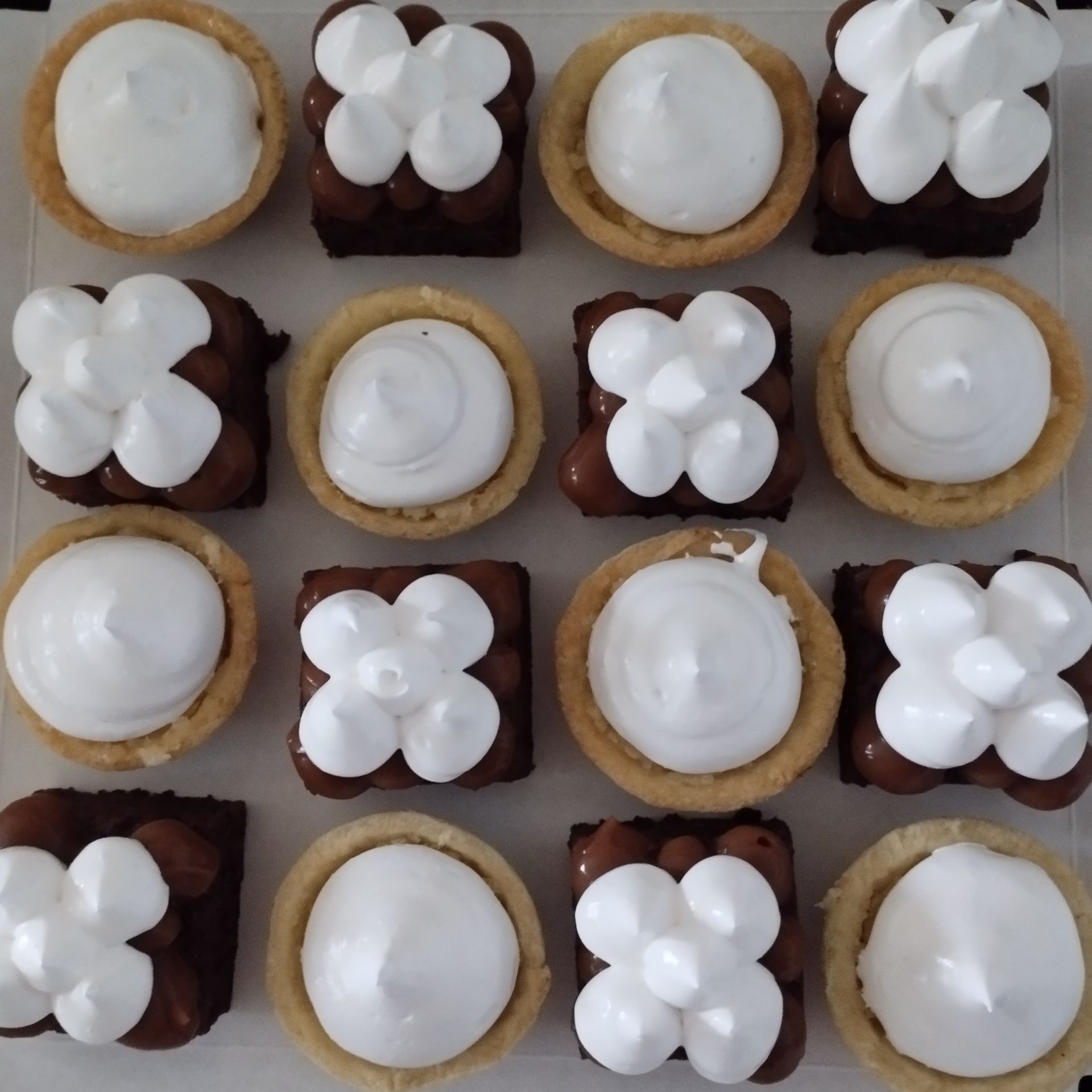 Surtido de magdalenas glaseadas con crema blanca y de chocolate, dispuestas en una cuadrícula ordenada.