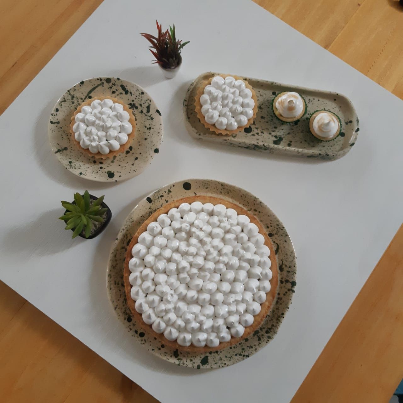 Tres platos de cerámica con postres blancos texturizados y pequeñas suculentas sobre una bandeja blanca.