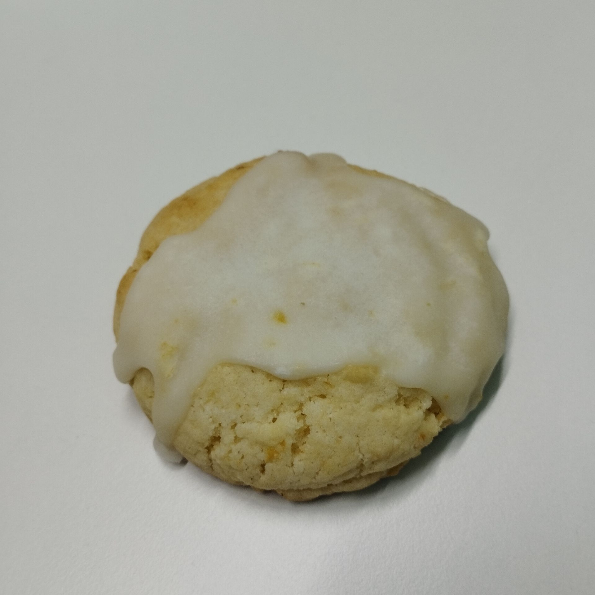 Galleta con glaseado blanco y base amarilla desmenuzable sobre un fondo claro liso.