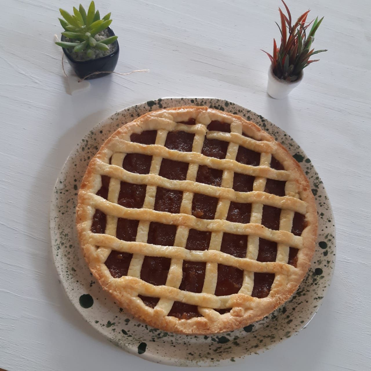 Tarta con rejilla en un plato moteado con dos pequeñas suculentas en maceta sobre una mesa blanca.