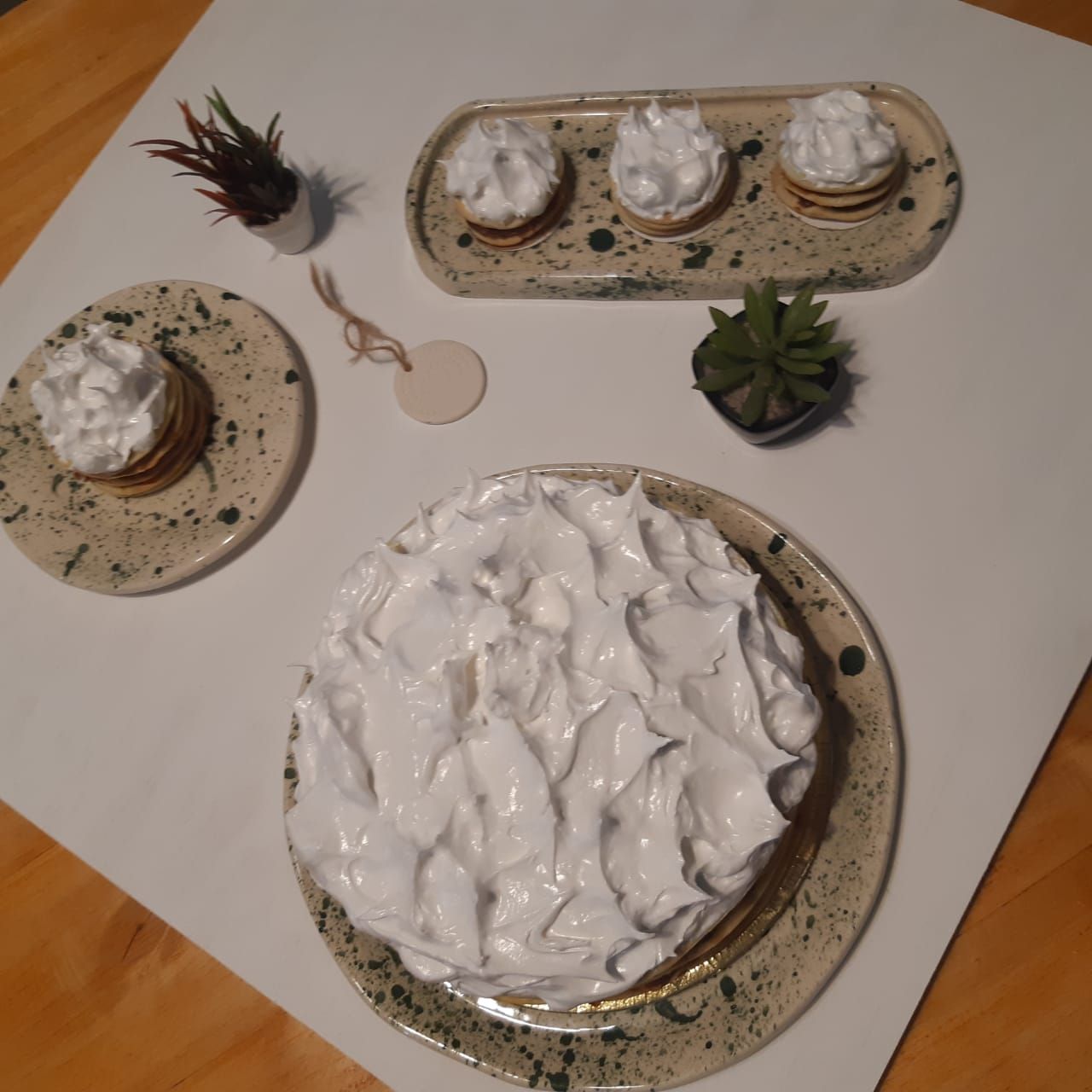 Mesa de postres con pasteles glaseados, cupcakes y pequeñas suculentas en platos decorativos.
