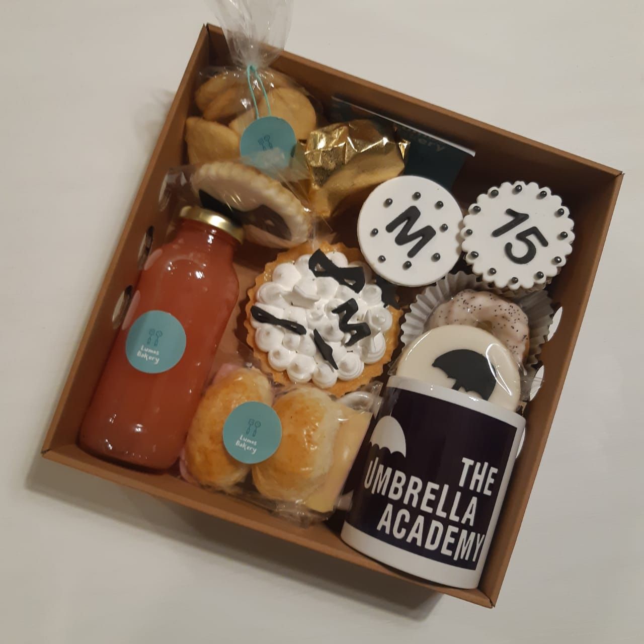 Caja de regalo con galletas, una botella de bebida roja y una taza negra con la etiqueta "The Umbrella Academy".