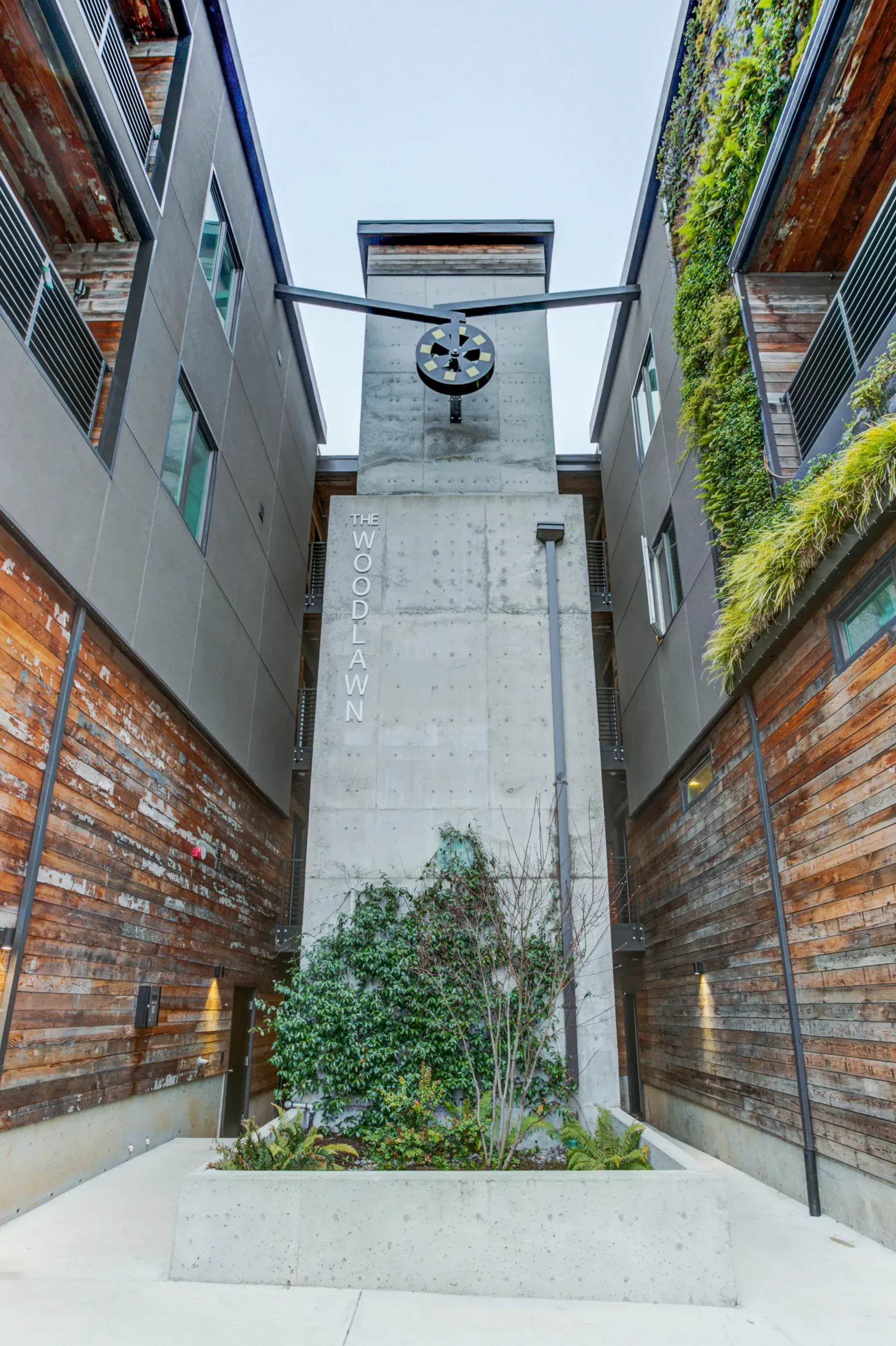 Narrow brick-lined courtyard with a tall concrete tower and a small central planter below a circular sign