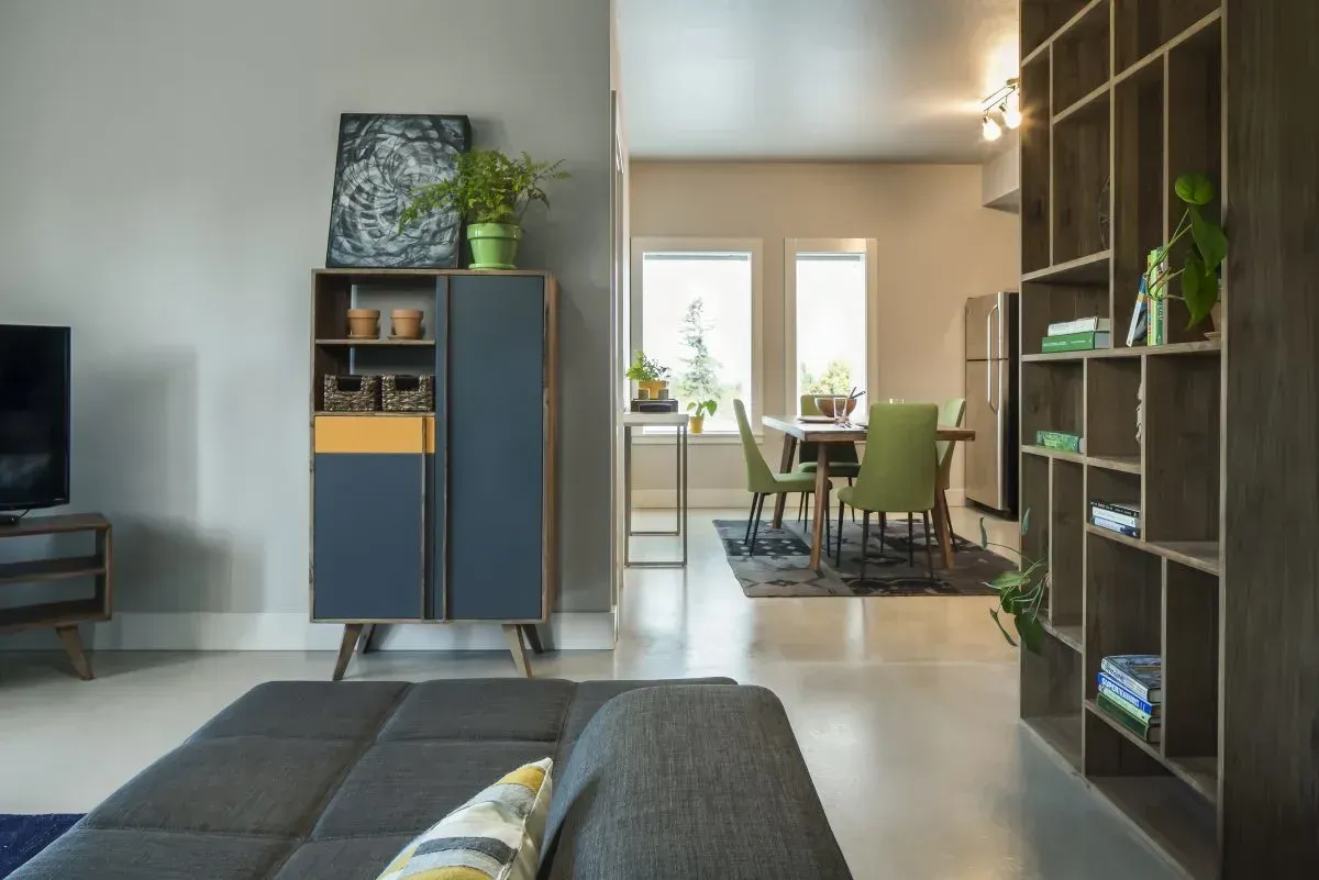 Modern living room with blue cabinet, dark sofa, and dining area by bright windows