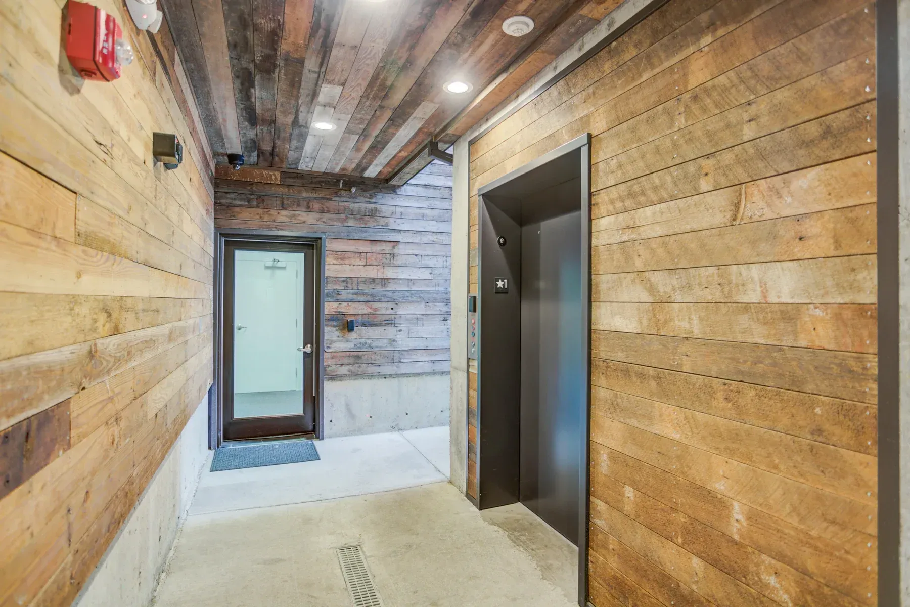 Narrow hallway with wood-paneled walls, exposed ceiling, and a doorway at the end.