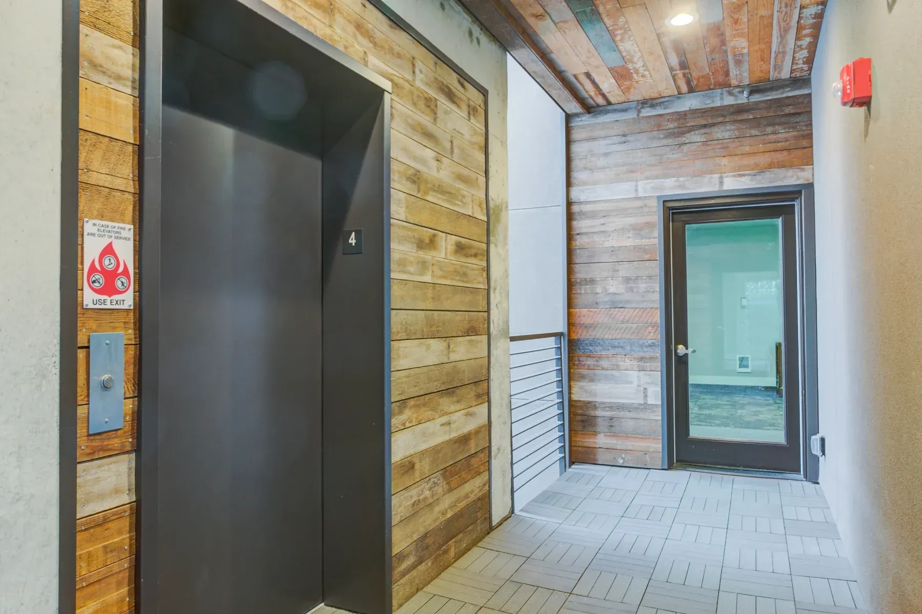 Empty elevator lobby with a closed dark elevator door, tiled floor, and hallway to a green door.