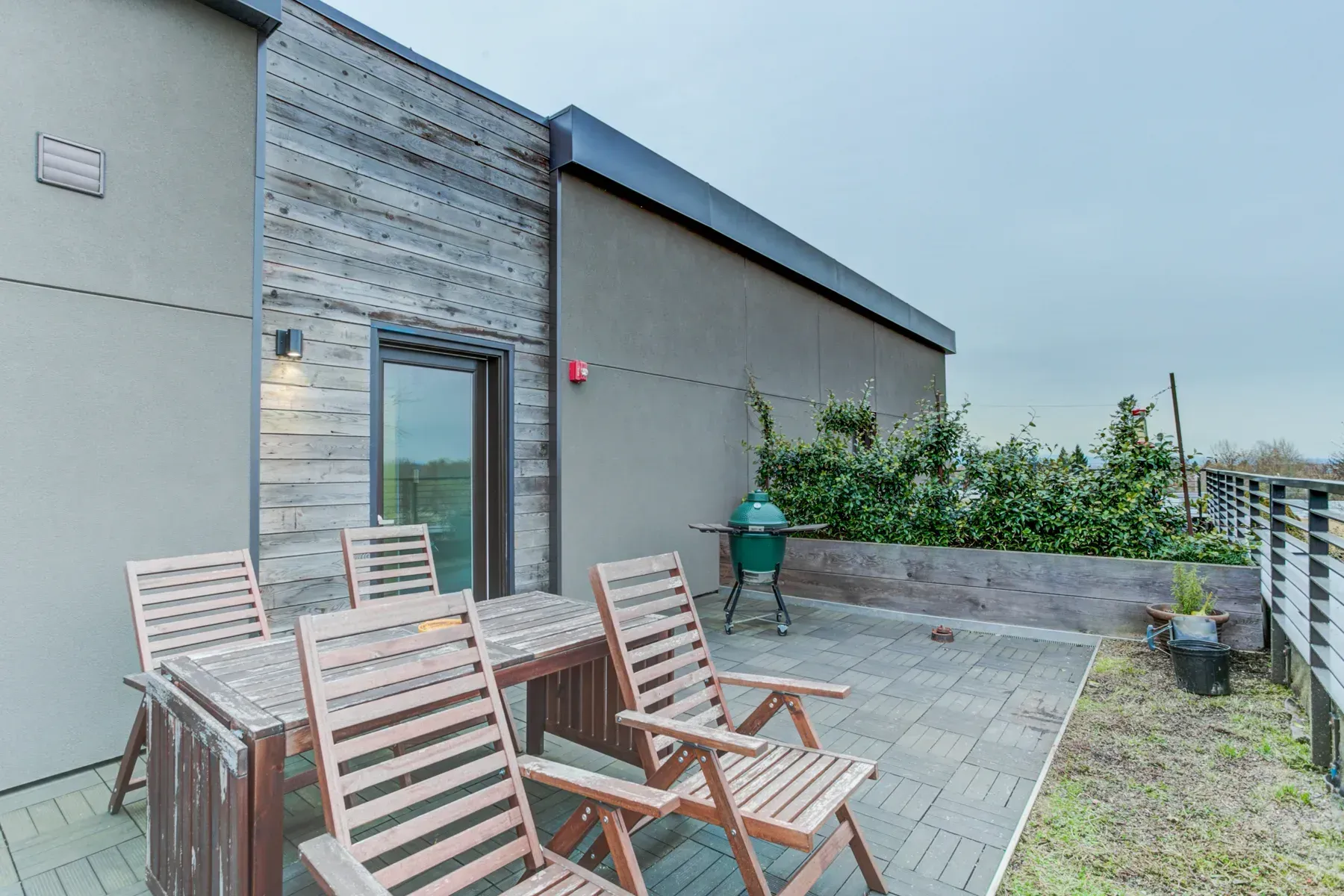 Patio with wooden chairs, a table, and potted plants beside a modern house.