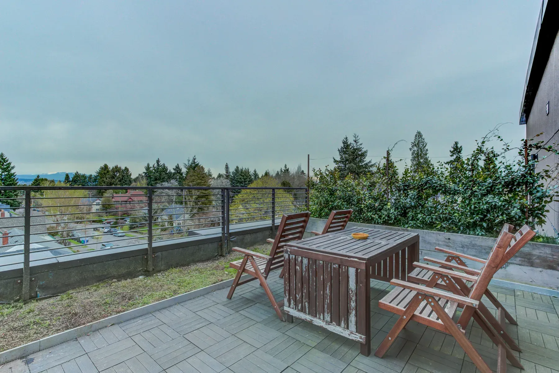 Patio with wooden chairs and table overlooking a fenced waterfront under a cloudy sky