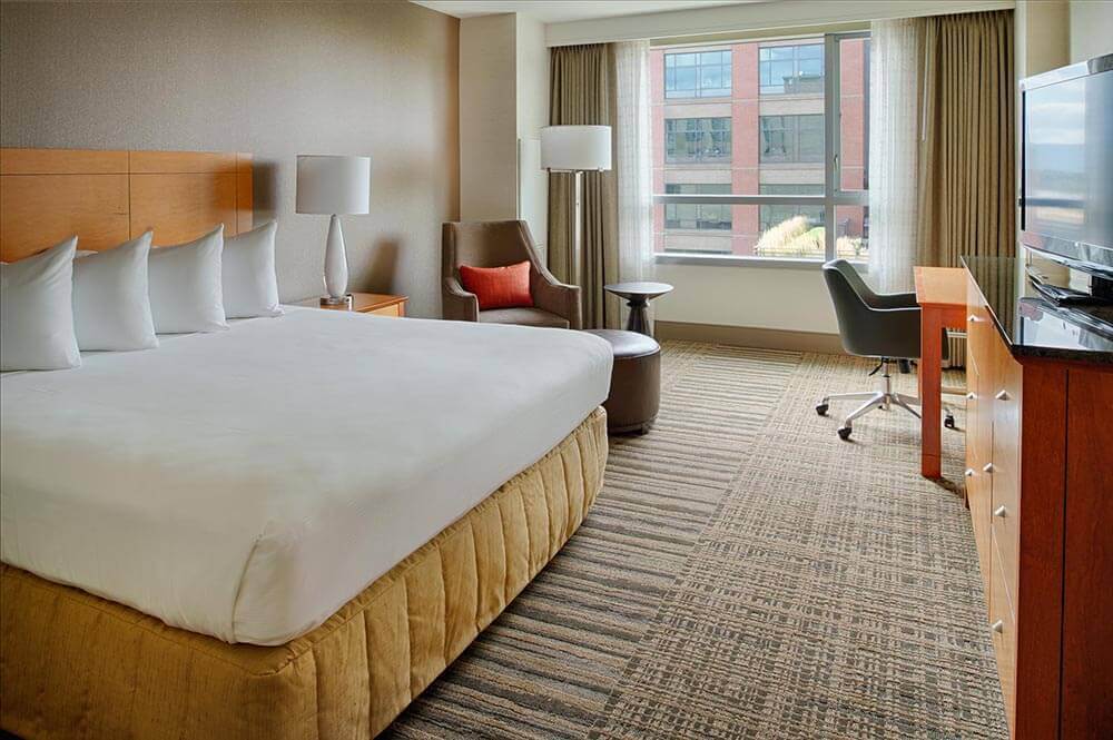 A hotel room with a king size bed , chair , desk and television.