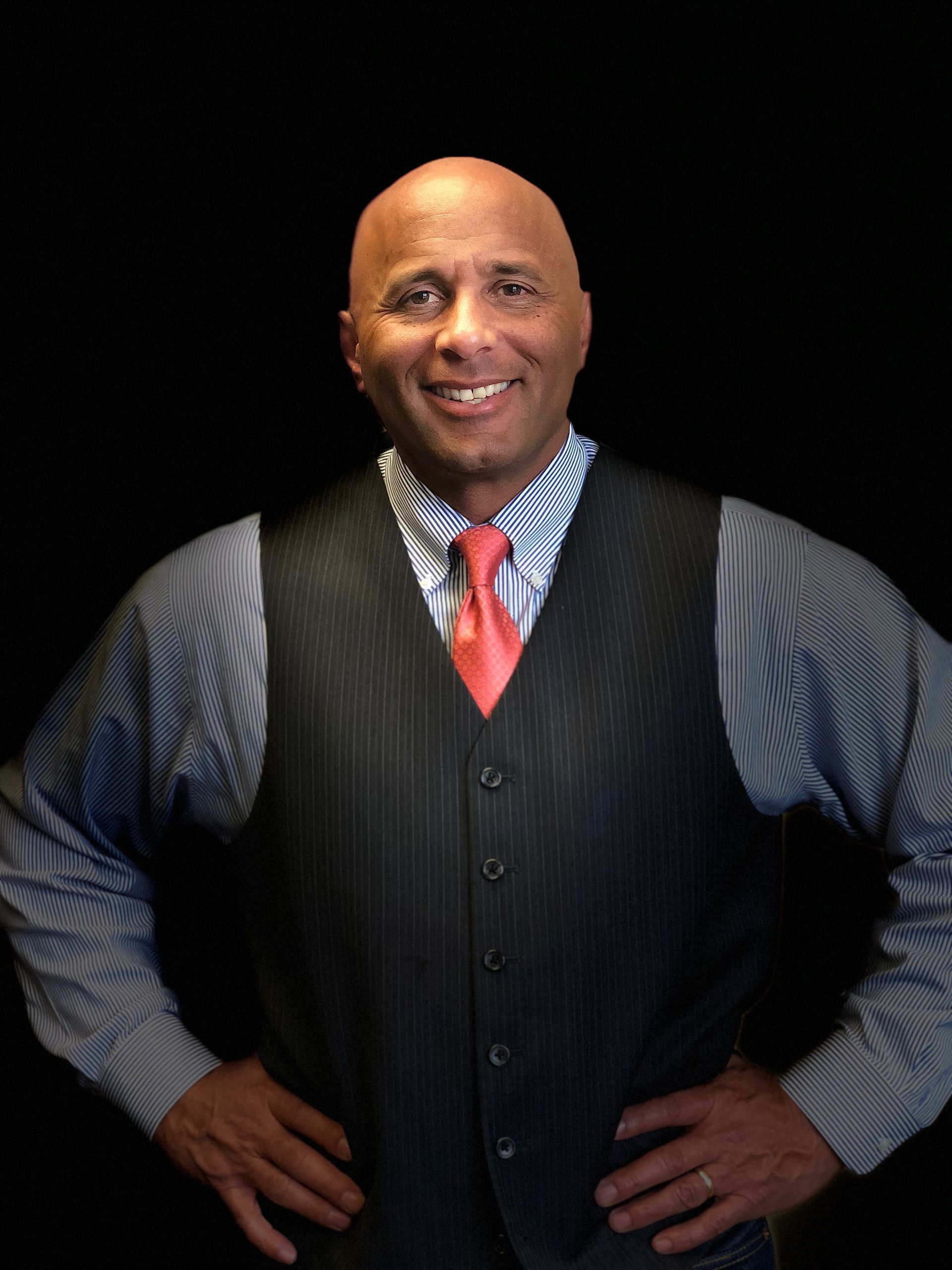 Dr Samuel Collins - Smiling man in a striped shirt, black vest, and red tie