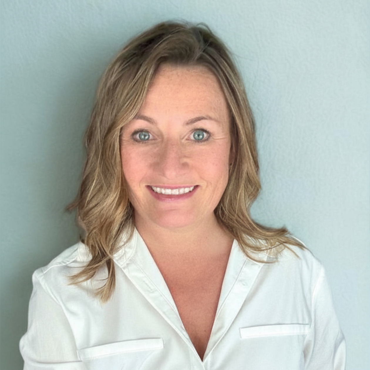Dr Jenna Davis - Smiling woman in a white blouse against a light blue background
