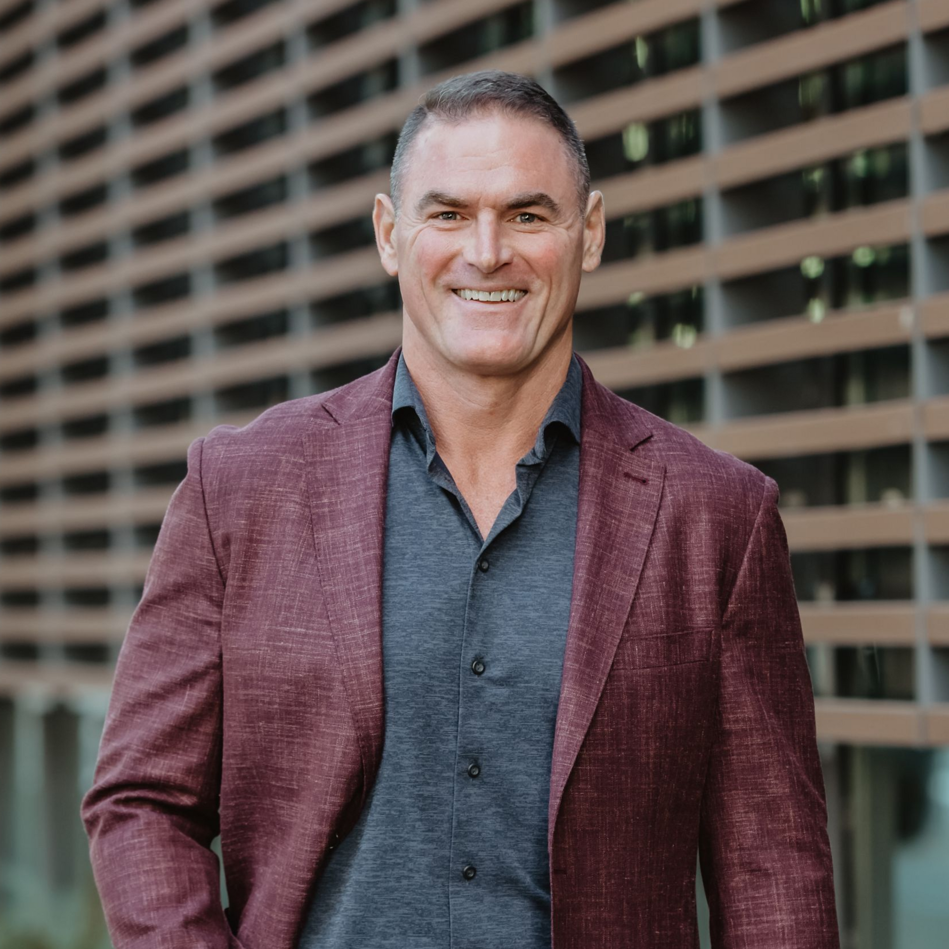 Dr. Paul Reed - Smiling man in maroon blazer and gray shirt standing outdoors against a modern building