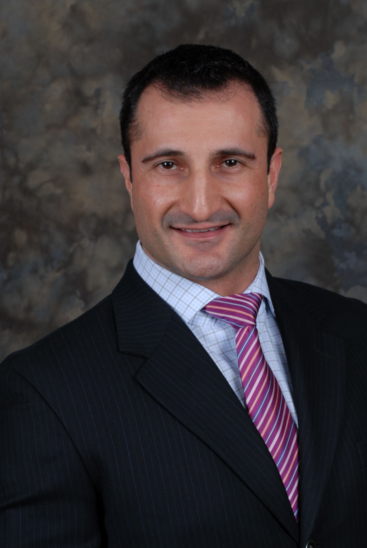 John Minardi - Formal studio portrait of a smiling man in a dark suit and pink striped tie