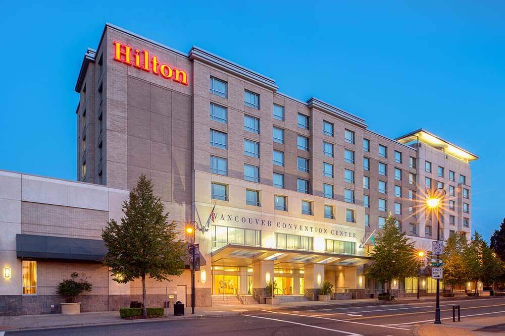 A large hilton hotel is sitting on the corner of a city street.