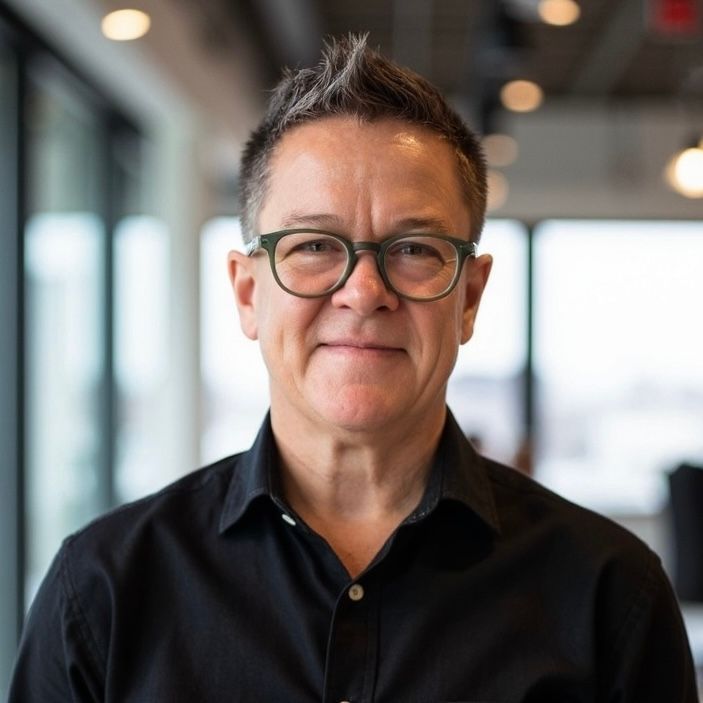 Dr. Monique Andrews - Portrait of a person wearing glasses and a black shirt, smiling in a softly lit office setting