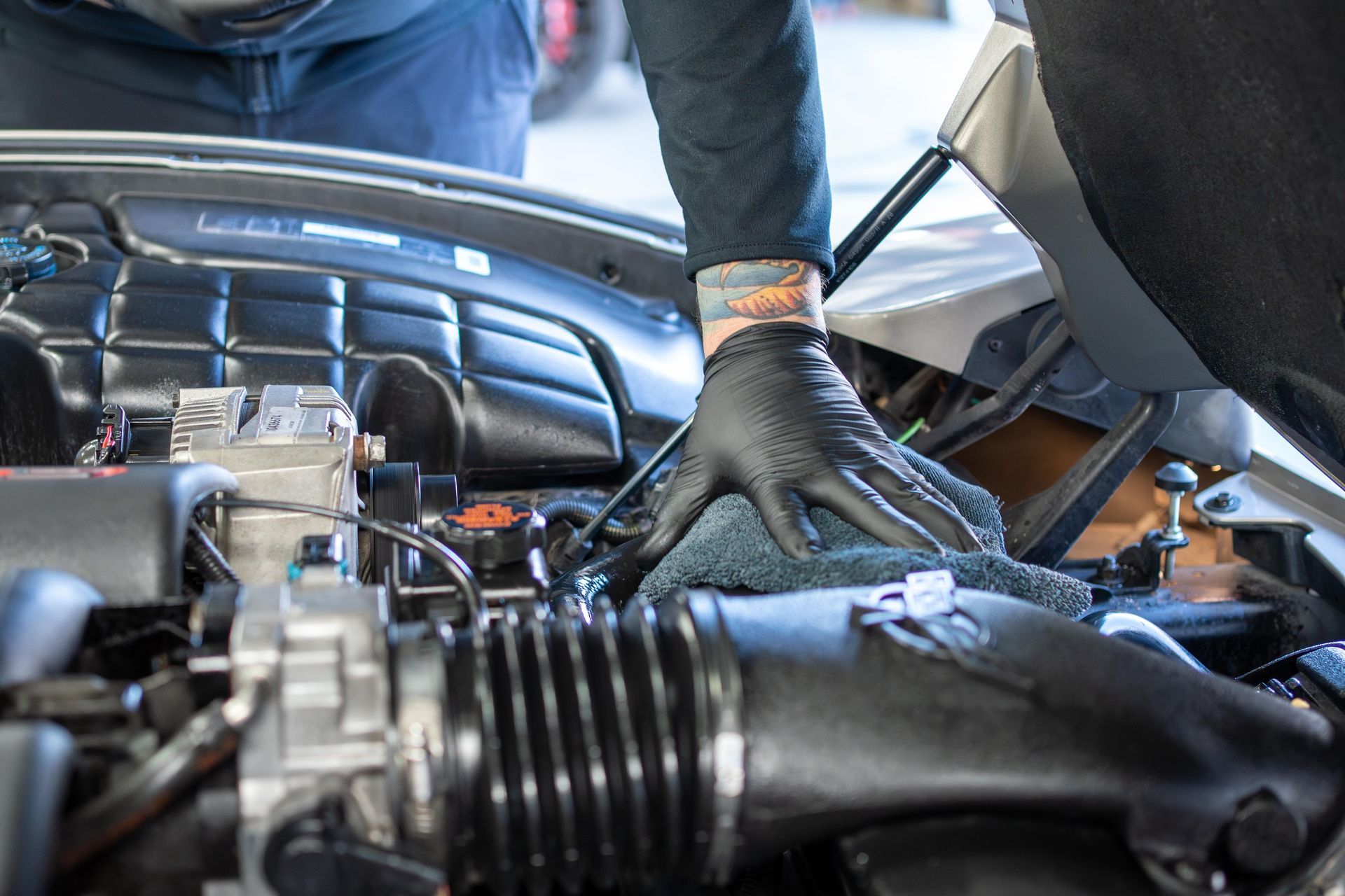 Person in black gloves cleaning a car engine with a cloth.
