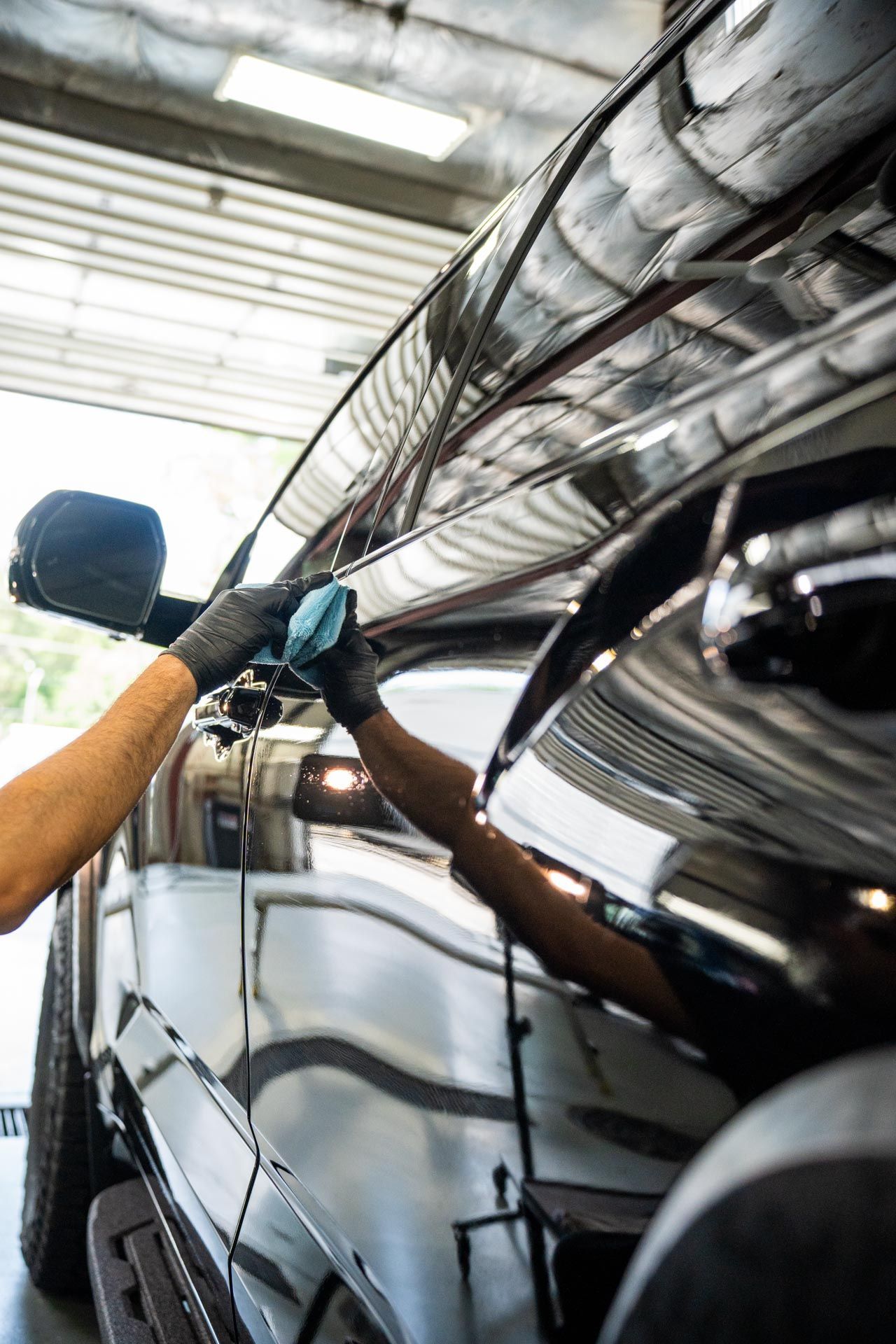 Person wearing black gloves wiping a shiny black car with a microfiber cloth, indoors.