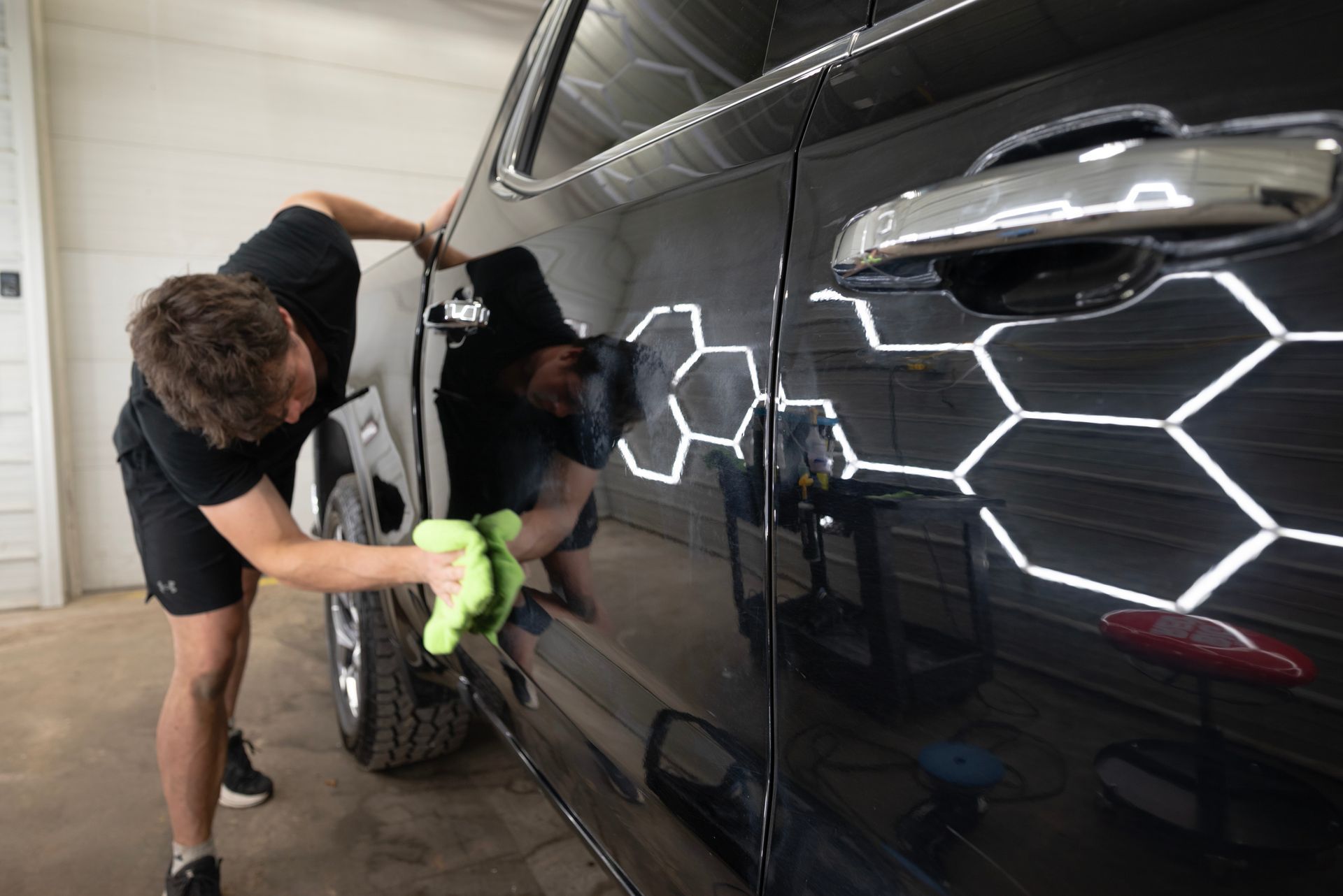 A person is wiping down a black truck with a green cloth in a well-lit garage.