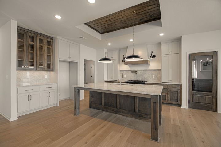 Bright white kitchen with island, wicker bar stools, pendant lights, and stainless steel appliances.
