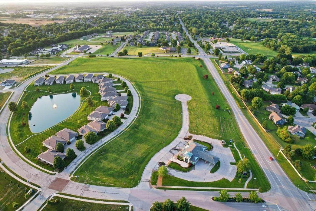 Aerial view of a suburban neighborhood with a pond, green parkland, roads, and houses.