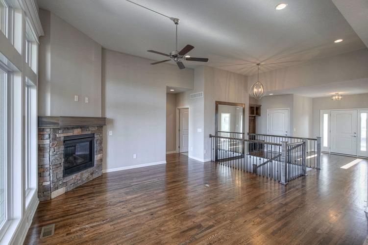 Bright open living room with hardwood floors, fireplace, ceiling fan, and staircase railing
