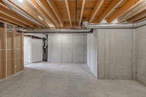 Empty unfinished basement with concrete walls and floor, exposed wooden ceiling joists, and utility area.