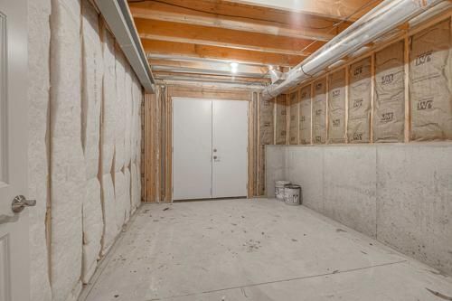 Unfinished basement with exposed insulation, white walls, and a central double door under wooden beams.
