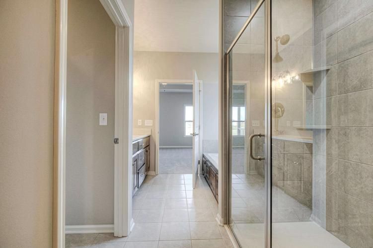 Modern bathroom with glass-enclosed shower, vanity, and light tile flooring leading to a doorway