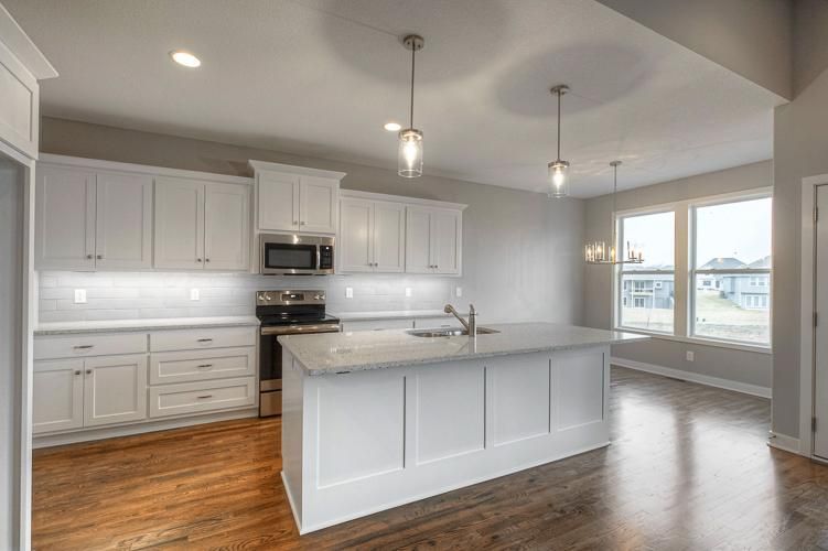 Bright modern kitchen with white cabinets, island, wood floors, and large window seating area