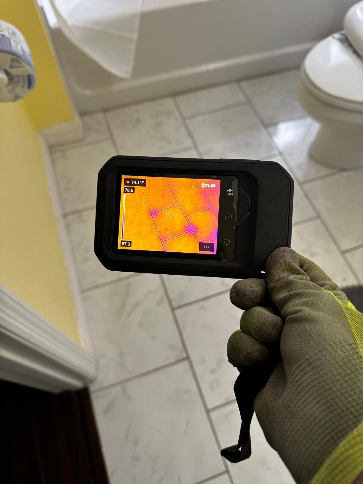 A person is holding a thermal camera in their hand in a bathroom.