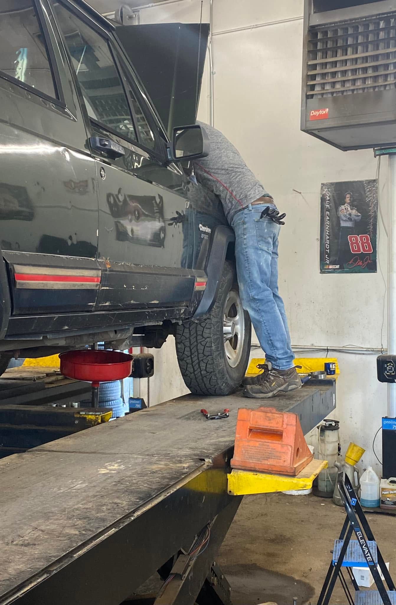 Mechanic working inside a gray SUV in an auto shop, standing on a ramp beside tools and equipment. | Cripple Creek Automotive Tire and Towing