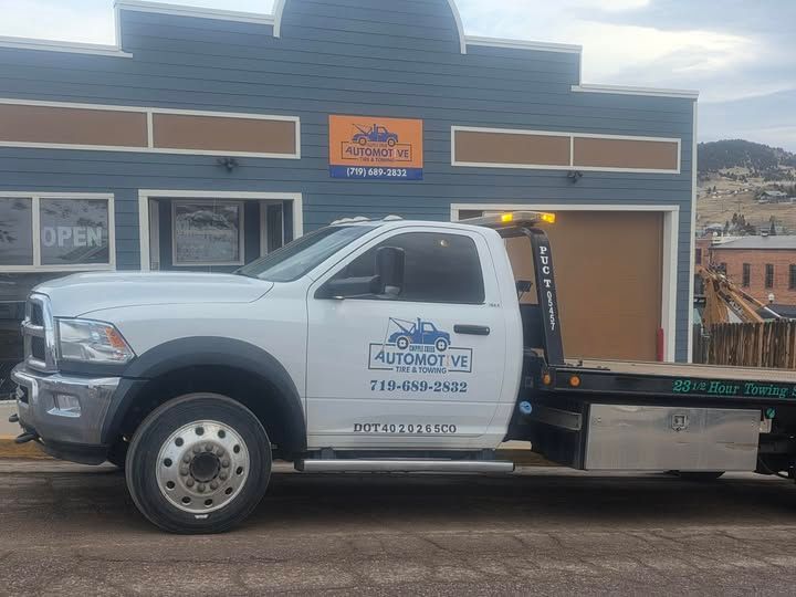 White tow truck parked in front of a building with a storefront sign and open door. | Cripple Creek Automotive Tire and Towing
