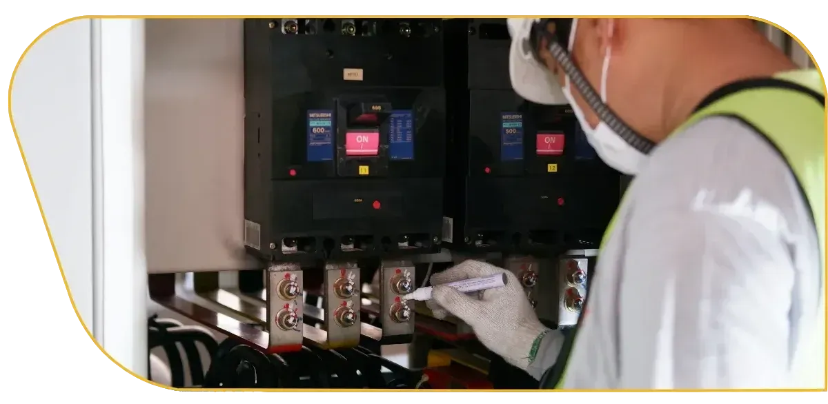 Technician inspecting electrical control panels inside a cabinet, wearing a safety vest and mask.