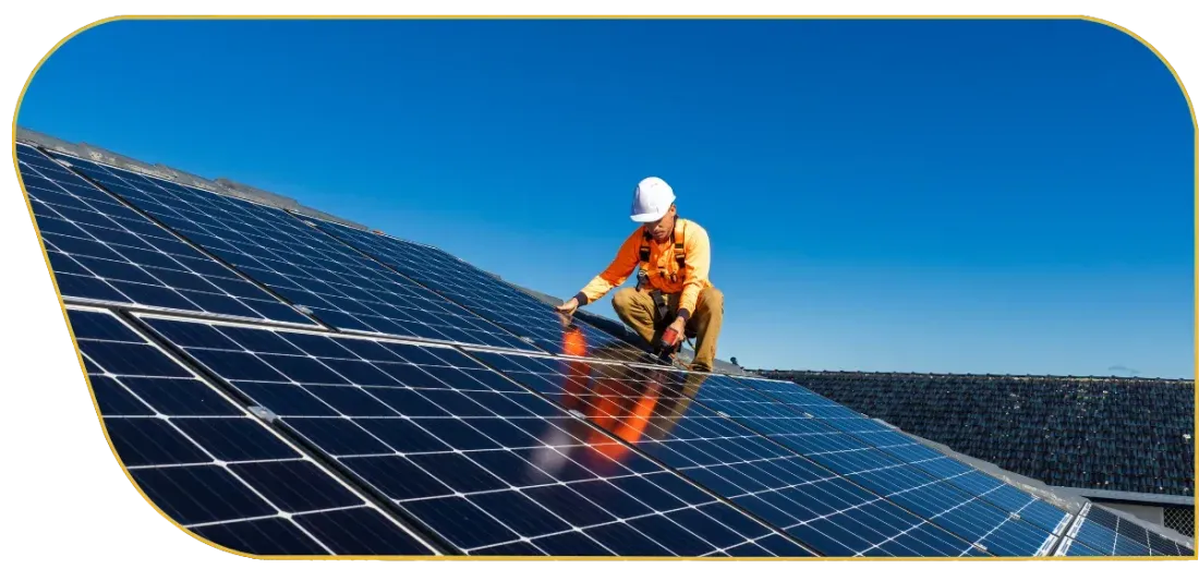 Worker in orange safety gear inspecting solar panels on a rooftop under a blue sky