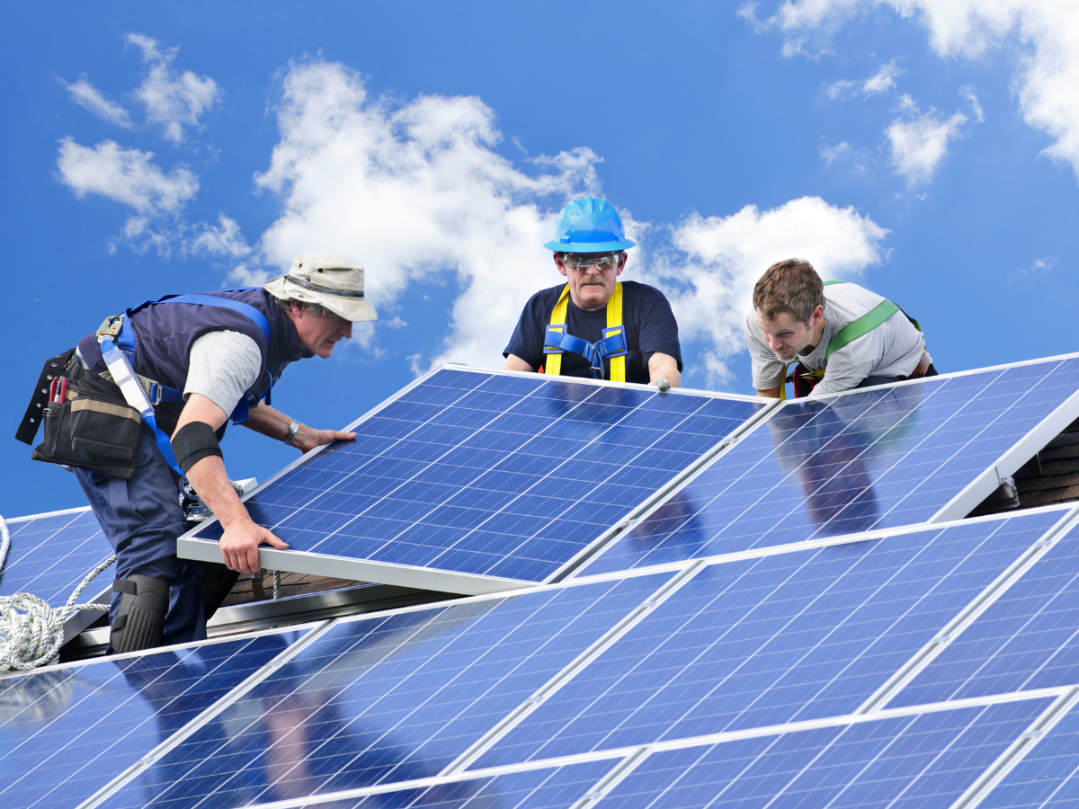 Workers installing solar panels on a rooftop under a blue sky