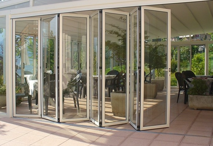 Folding glass doors, open to a patio with tables and chairs, under a white awning.