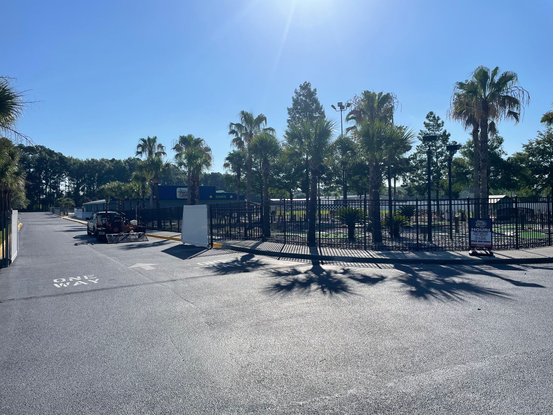 A parking lot with a fence and palm trees on a sunny day