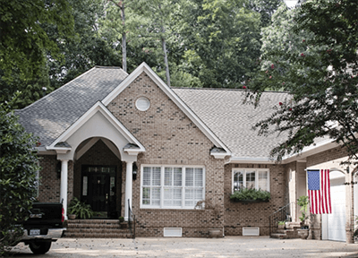 Brick suburban house with arched entry, white shutters, and an American flag by the driveway