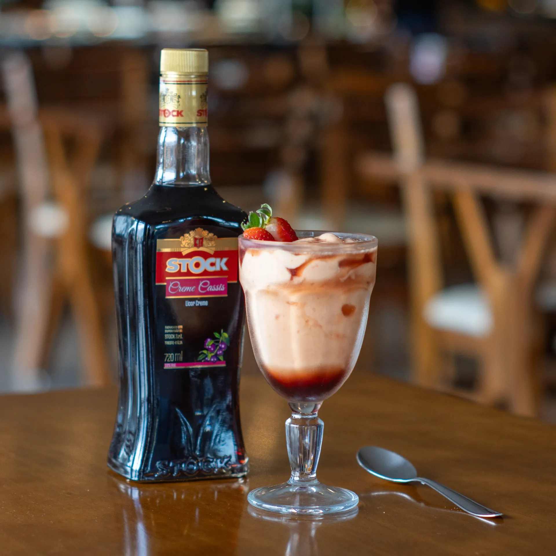Garrafa de licor Stock Creme Cassis ao lado de uma sobremesa em camadas com uma colher sobre uma mesa de madeira. Chalé Mont Hermon.