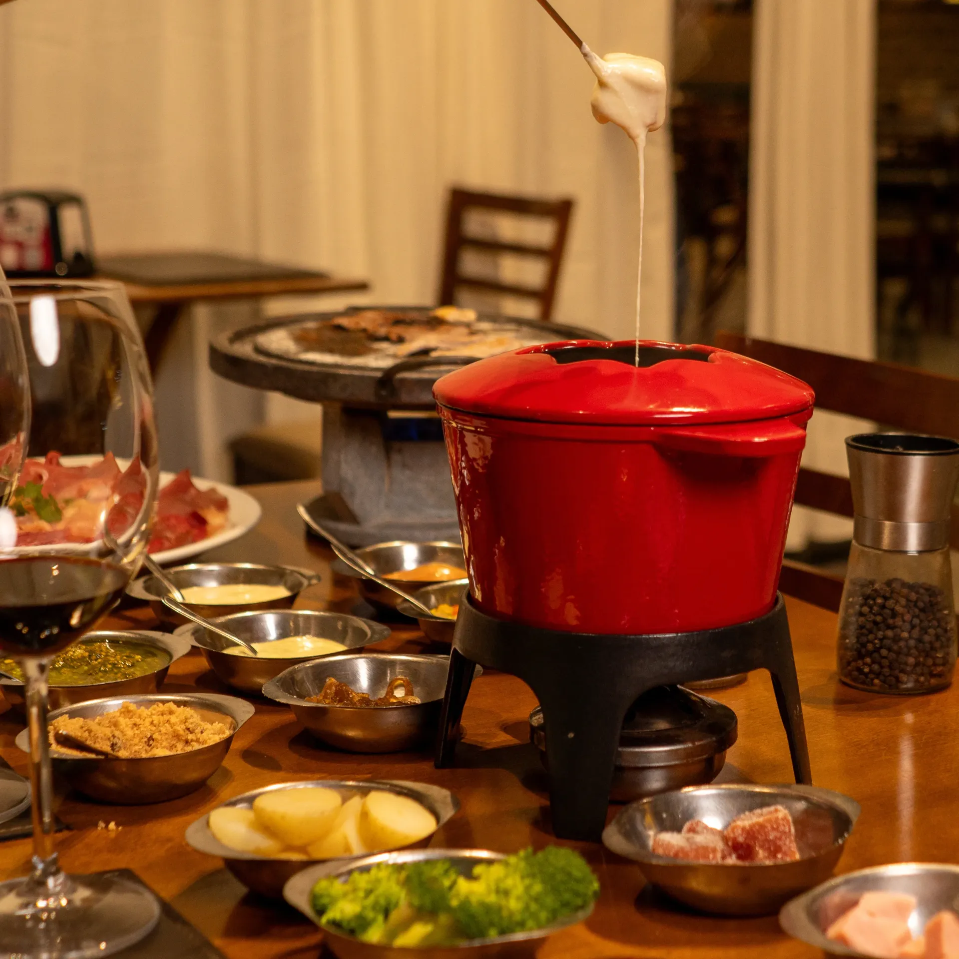 Um jantar de fondue com uma panela vermelha e vários itens para mergulhar em uma mesa de madeira. Chalé Mont Hermon.